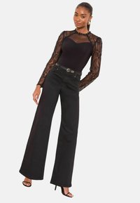 Fekete testhezálló ruha hosszú csipkés ujjakkal és tengericsipke részletekkel az oldalán, magasított derekú, bővülő fekete farmernadrággal és fekete magas sarkú szandállal párosítva.