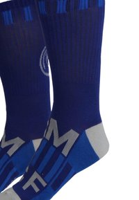 Calze blu con texture a coste, caratterizzate da un design geometrico in varie tonalità di blu e grigio, e con la scritta "MF" in grassetto vicino alla punta.