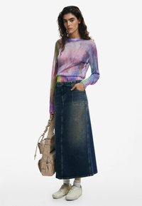 Langarm, meerkleurig gebreid top met een gradient patroon, gecombineerd met een donkerdenim maxi rok en lichte sneakers, terwijl ze een beige handtas vasthoudt.