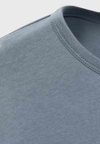 Ljusblå bomull T-shirt med rund halsringning, mjuk textur och diskreta söm detaljer längs kragen och axelsömmarna.