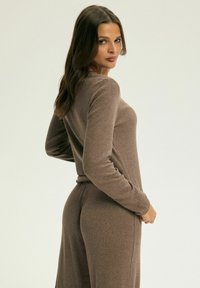 Brązowa dzianinowa odzież do noszenia w domu z długimi rękawami, dopasowanym fasonem i elastyczną talią. Miękka faktura i gładka tkanina o lekkim wyglądzie.