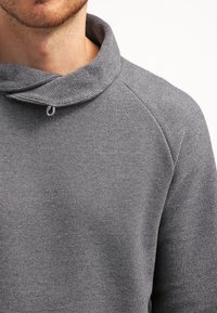 Harmaa neulepusero, jossa on kauluksessa kaula-aukko, valmistettutekstuurista neulekangasta. Ominaisuuksina raglan-hihat ja silmukkakoriste kaula-aukossa.