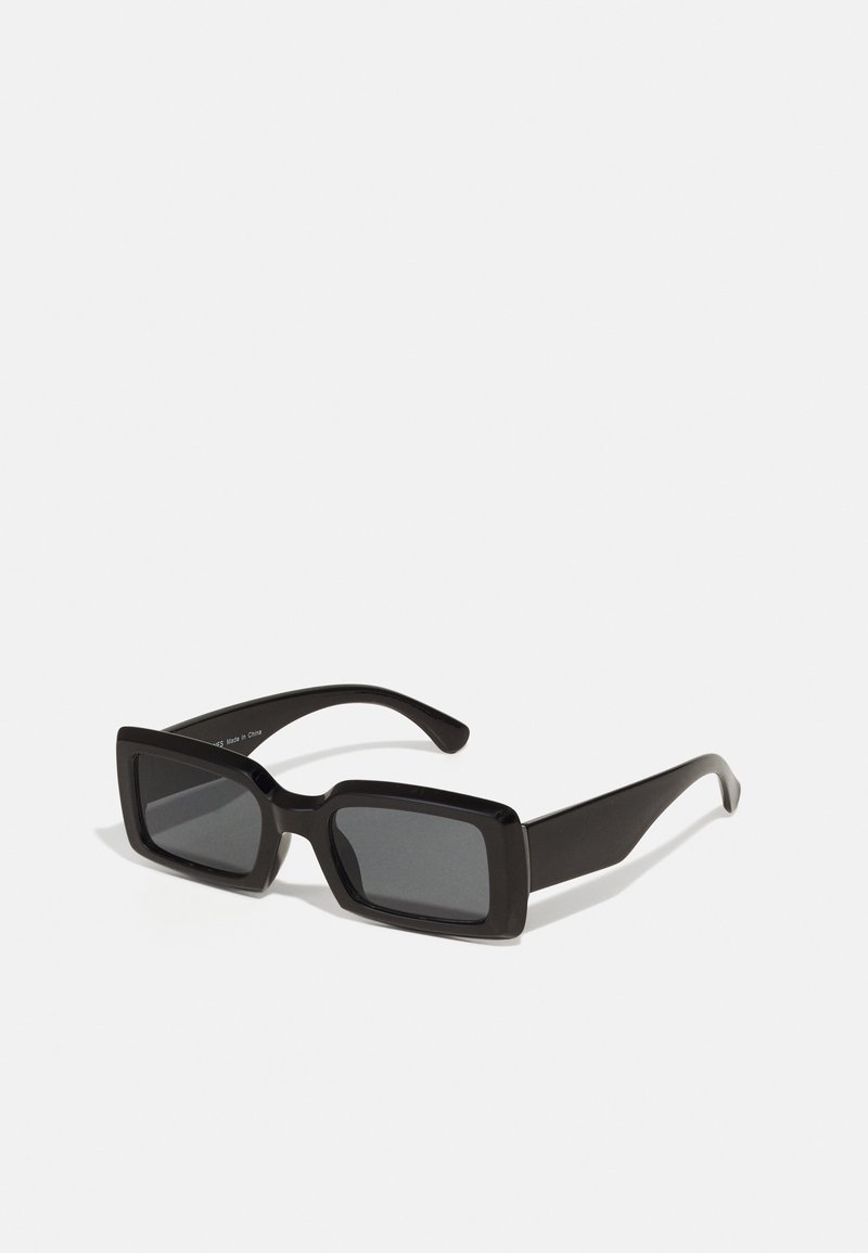 Lunettes de soleil noires rectangulaires avec des verres foncés. Monture en plastique épaisse et brillante avec des branches droites et un design minimaliste.