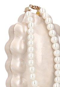 Bílý perlový náhrdelník přehazený přes strukturovaný, světle růžový povrch ve tvaru mušle s lesklým povrchem a zlatým kováním.