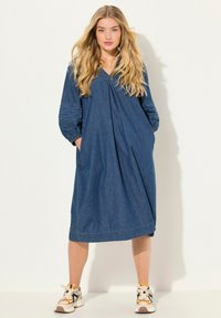 Denim midi-mekko, jossa on V-pääntie, laskostettu yläosa, pitkät brodeeratut hihat ja sivutaskut. Yhdistetty massiivisiin lenkkareihin.