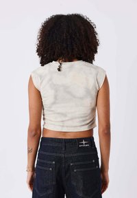 Haut court à manches courtes en tie-dye beige clair, associé à un jean en denim foncé taille haute avec un logo brodé à l'arrière.