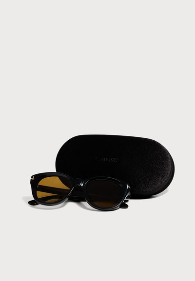 Lunettes de soleil rectangulaires noires avec des verres marron foncé reposant devant un étui dur ovale noir sur fond blanc.