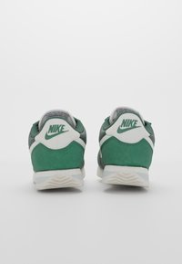 Zelene i bijele Nike tenisice s nubuk gornjištem, podstavljenim ovratnikom i ikoničnim logotipom na peti, s teksturiranom gumenom podlogom.