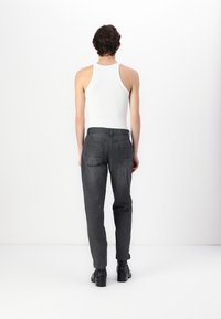 Pantaloni grigi a sigaretta con tasche posteriori, abbinati a una canotta bianca, che mostrano un design semplice e un taglio classico. Calzature nere completano il look.