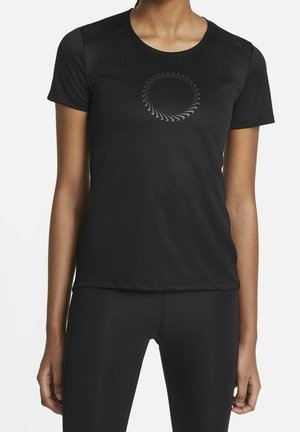 Frau trägt ein schlichtes schwarzes athletisches Kurzarmshirt mit einem kreisförmigen strukturierten Wirbel-Design in der Mitte der Brust.