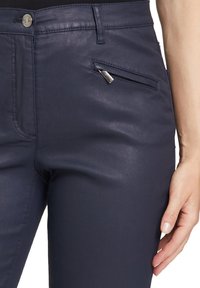 Dunkelmarineblaue Hosen aus einem glatten, dehnbaren Stoff, mit einer Reißverschlusstasche auf der rechten Seite und einem klassischen Knopfverschluss.