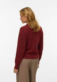 Ribaga burgundia kampsun tekstuursete pom-pom detailidega, ümar kaelus ja pikad varrukad, kantud heledate pruuni vabade pükstega.