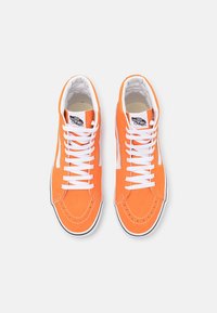 Vysoké tenisky v jasně oranžovém semiši s bílými tkaničkami, kontrastním bílým pruhovaným bočním zdobením a černým lemováním kolem podešve.