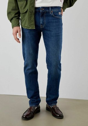 Jeans blu scuro con vestibilità slim, realizzati in denim, con cinque tasche, lievi sfumature e dettagli di cuciture marroni. Abbinati a scarpe nere.