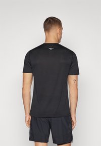 Camiseta deportiva negra con cuello redondo, mangas cortas y un logotipo reflectante en la parte superior de la espalda. Fabricada con un tejido ligero y transpirable.