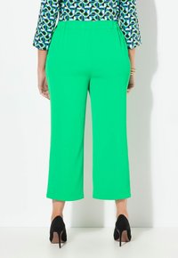 Zelené, široké kalhoty z lehkého materiálu s hladkým vzhledem, které mají pohodlný elastický pas a zkrácenou délku.