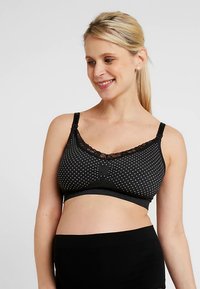 Sutiã de maternidade preto com bolinhas brancas, com acabamento em renda, tecido suave, alças ajustáveis e textura tricotada. Apresenta um laço central como detalhe.