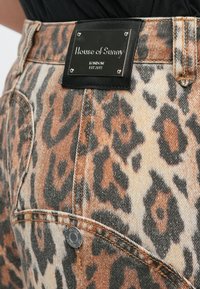 Τζιν σορτς με λεοπάρ εκτύπωση και μαύρη ετικέτα από συνθετικό δέρμα, με ασημένιο λογότυπο και στρογγυλά μεταλλικά στοιχεία. Το ύφασμα έχει υφή με ανάγλυφο φινίρισμα.