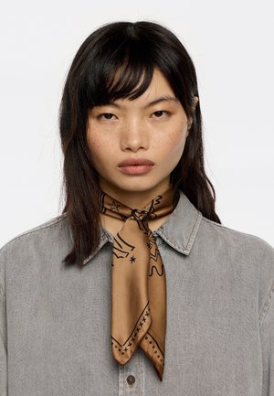 Brąszowy jedwabny szalik z czarnymi wzorami graficznymi, związany wokół szyi. Model ma na sobie jasnoszary dżinsowy koszula z kołnierzykiem.