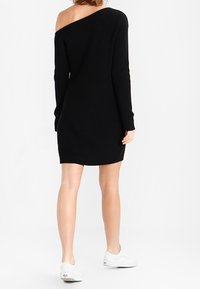 Schwarzes, schulterfreies Strickkleid mit langen Ärmeln, geripptem Textur und taillierter Silhouette, getragen mit weißen Sneakers.