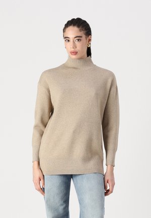 Pull en col roulé beige en tissu doux, avec des poignets et un ourlet côtelés, un ajustement décontracté et un design minimaliste.