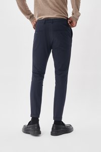 Pantalons ajustés bleu marine avec une coupe slim, ourlets retroussés et deux poches arrière, portés avec des chaussures noires à enfiler, sur fond blanc.