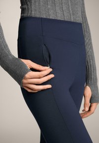Tengeri kék leggings rugalmas anyagból, oldalt cipzáras zsebbel és magas derékrésszel. A modellen egy szürke bordázott pulóver látható.