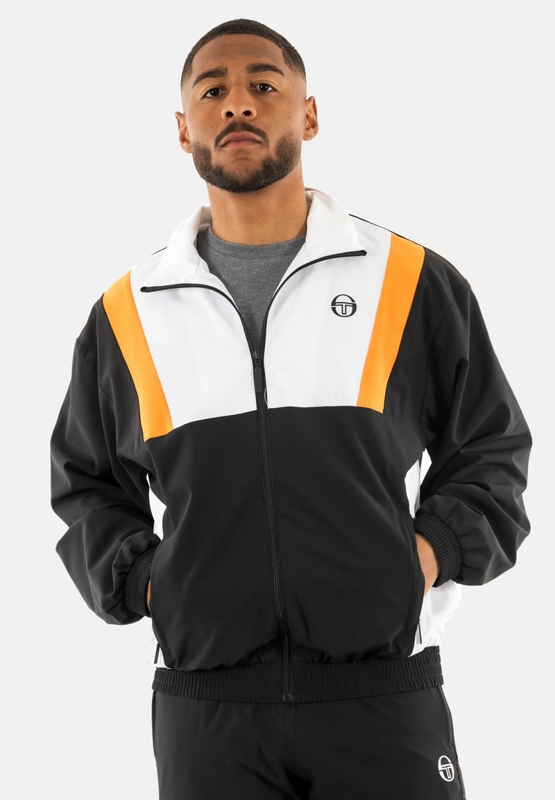 Chaqueta de cremallera en blanco y negro con franjas naranjas en los hombros, un logo redondo en el pecho, puños elásticos y un corte relajado.