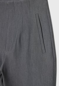 Gros plan sur un pantalon gris sur mesure montrant une poche fendue verticale et des coutures détaillées sur le tissu.