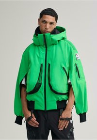 Neon grüne, übergroße Jacke mit hohem Kragen, Reißverschlusstaschen und kontrastierenden schwarzen Akzenten. Hergestellt aus glattem, strapazierfähigem Material.