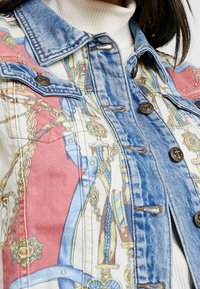 Veste en denim dotée d'une impression graphique colorée avec des chaînes et des motifs. Col bleu, fermetures à boutons et coutures détaillées.