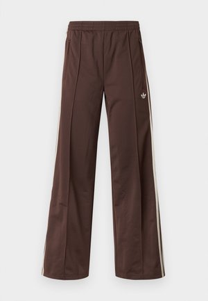 Bruine sportbroek met een wijd uitlopende pijp, witte zijstrepen, een elastische tailleband en twee zijzakken. Heeft een klein logo op het been.