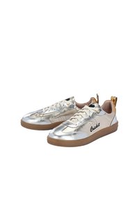 Sneaker metallici argento con una superficie liscia, suola in gomma marrone, lacci bianchi e un accento dorato sul tallone, con il marchio "Cricket".
