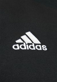 Un tessuto nero presenta un logo Adidas ricamato bianco, che mostra tre strisce angolate e il nome del marchio in lettere minuscole.