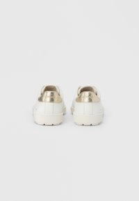 Λευκά αθλητικά παπούτσια με ανάγλυφη χρυσή λεπτομέρεια στη φτέρνα, με ομαλή σχεδίαση και ελαφριά σόλα, κατάλληλα για casual χρήση.