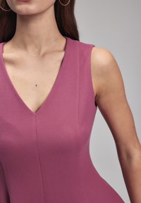 Débardeur à col en V sans manches en tissu mauve texturé, présentant une coupe ajustée avec des lignes épurées et sans fermetures ni embellissements visibles.