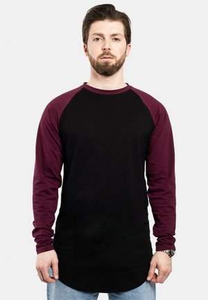 Schwarzes Langarmshirt mit kastanienbraunen Raglanärmeln, Rundhalsausschnitt und abgerundetem Saum. Aus weichem Baumwollmaterial mit taillierter Passform.