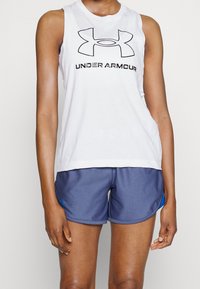 Canotta atletica bianca senza maniche con logo "UNDER ARMOUR" nero, abbinata a pantaloni corti blu navy con un accento laterale blu.