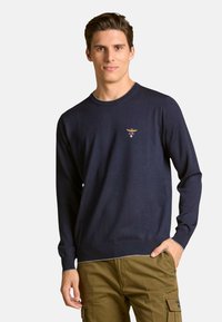 Suéter de punto azul marino con mangas largas y cuello redondo, con un pequeño logo bordado en el pecho. Textura suave, ajuste casual.