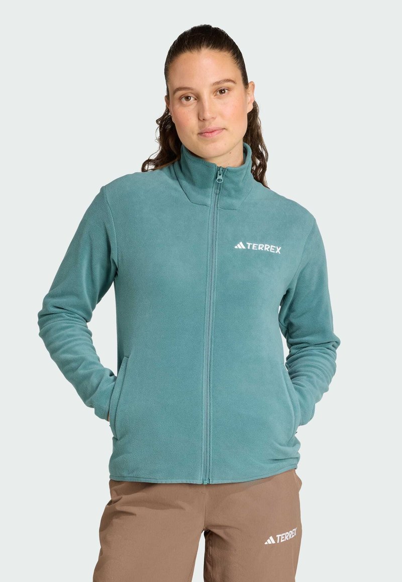 Giacca in pile di colore teal, con colletto alto e zip frontale. Logo sul petto. Tessuto morbido con maniche lunghe e tasche laterali.