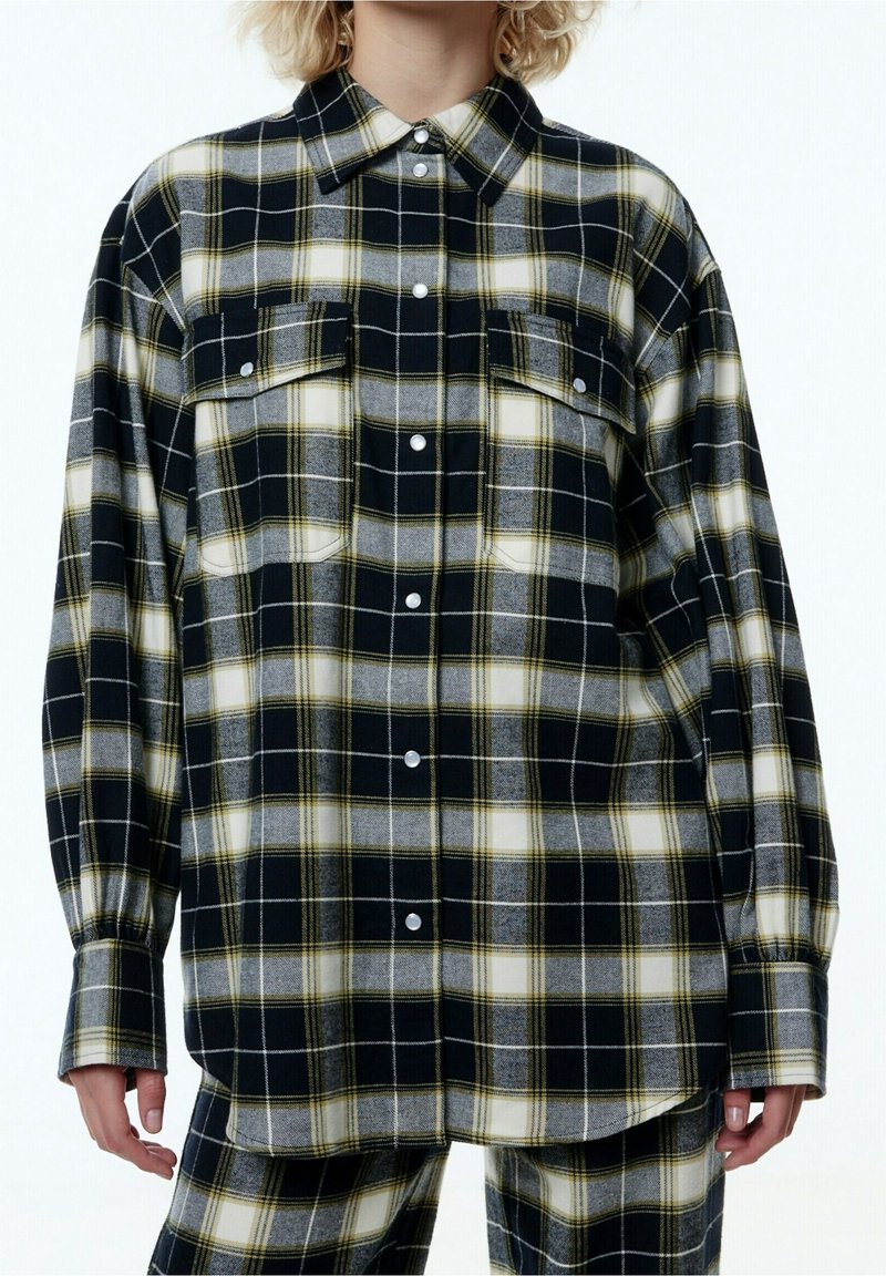 Karierter Button-up-Hemd in Schwarz, Grau und Gelb mit lockerer Passform, zwei Brusttaschen und abgerundetem Saum. Hergestellt aus weichem, wollähnlichem Material.