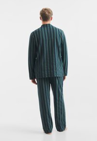 Pruhovaný pyžamový set v tmavě modré barvě s vertikálními zelenými a červenými pruhy, se topem bez límečku a volnými kalhotami. Jemná tkanina.