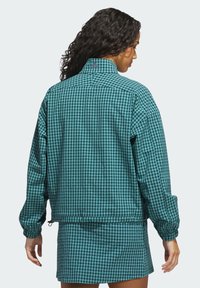 Tealternet ternet blazer med lange ærmer, en ståkrave og elastiske manchetter; har en snor i kanten og et minimalt logo på bagsiden.