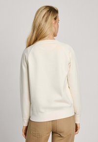 Felpa leggera beige con maniche lunghe e colletto a girocollo. Realizzata in materiale morbido, con polsini e orlo a costine. Design minimalista.