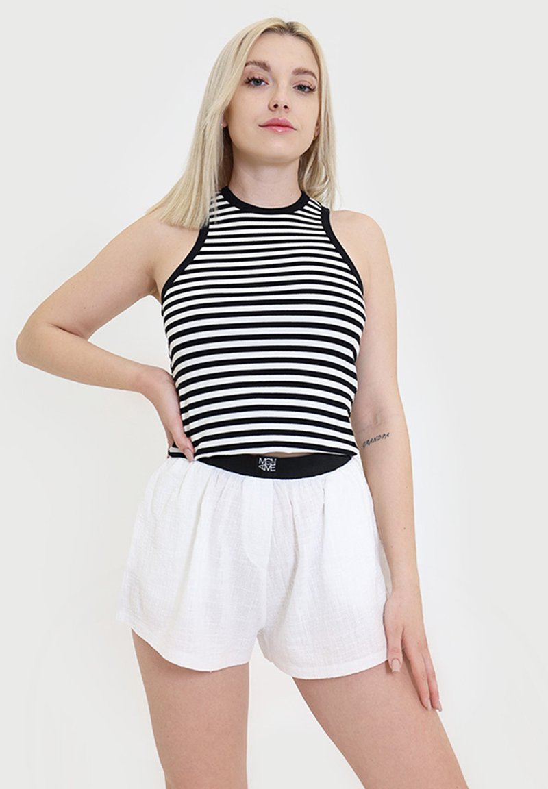 Czarnobiała w paski bezrękawnik w zestawieniu z białymi, lekkimi, teksturowanymi szortami. Strój charakteryzuje się dopasowanym krojem i swobodnym stylem.