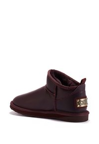 Botas de tobillo de cuero burdeos con un suave forro interior, punta redonda y un acento dorado de marca en el tacón. Presenta un diseño cosido.