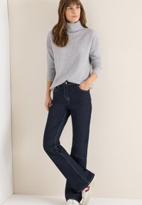 Szary dzianinowy sweter z golfem i ciemnoniebieskie dzwony z kontrastującym przeszyciem, zestawione z białymi tenisówkami z czerwonymi akcentami.