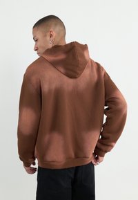 Hanorac maro cu o croială relaxată, având glugă cu șnur, manșete și tiv cu canal. Textură netedă, design simplu, fără modele vizibile.