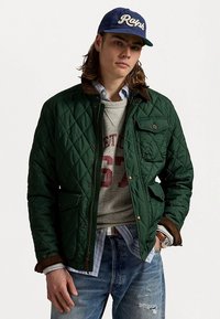 Žalia siuvinėta striukė su rudu korduro pagrindiniu apykaklė, priekyje užtrauktuku ir krūtinės kišene. Dėvima ant pilkos džemperio su bordo spalvos užrašu ir mėlynos spalvos languoto marškinių.