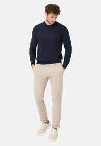 Marine gebreide trui, beige chino's en lichte sneakers. De chino's hebben een slim fit, de trui heeft geribbelde manchetten en onderkant voor extra textuur.